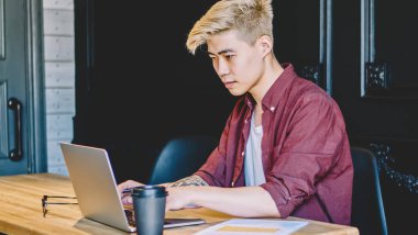 Modern uzayda kablosuz internet bağlantısı kullanarak dijital dizüstü bilgisayarda serbest çalışan düşünceli Japon genç adam. Mesafeli iş için bilgisayara uygulama yükleyen konsantre Asyalı hipster.