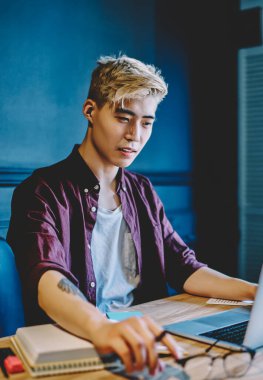 Gündelik giysiler giymiş yaratıcı Japon grafik tasarımcısı modern dizüstü bilgisayardaki internet sitesinde kablosuz internet kullanıyor. Netbook 'ta oturan ve serbest çalışan Çinli genç adam