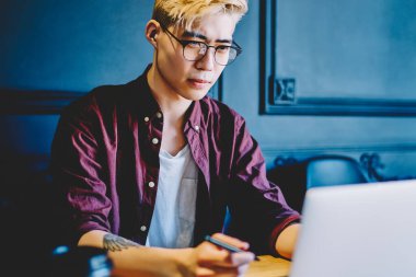 Çinli bir adam bilgisayar aygıtında program kodu oluşturmak için serbest çalışan yeni bir uygulama yüklüyor. Hippi adam internet bağlantısı kullanarak internet üzerinden webinar izliyor.