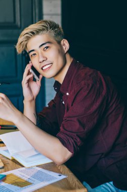 Başarılı Çinli hipster IT geliştiricisinin portresi internet üzerinden akıllı telefondan arama yaparken internet üzerinden kablosuz internet kullanıyor. Cep telefonuyla konuşan pozitif Japon genç adam.