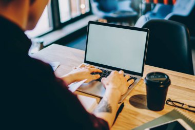 Ders bilgileri için dizüstü bilgisayarda yazı yazan yenilikçi öğrencilerin arka plandaki görüntüsü kahve dükkanındaki ahşap masada otururken internet sitesi için boş ekran alanı olan bir bilgisayar.