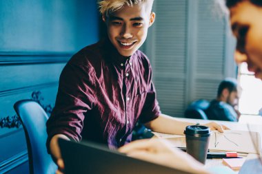 Neşeli sarışın Japon hipster öğrenci ve kız arkadaşı dizüstü bilgisayar ekranında tasarım skecini izliyorlar ve modern çalışma alanındaki işbirliği sürecinde projeyi analiz ediyorlar.