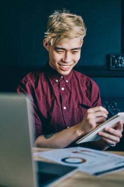 Neşeli Çinli adam kitabı elinde tutuyor ve notlar alırken kağıttan grafikler alıyor. Mutlu gülümseyen Japon hipster öğrenci defterine çizim çiziyor ve dizüstü bilgisayarla modern uzayda oturuyor.