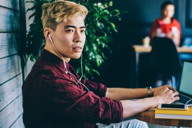 Loft iç kafeteryadizüstü cihaz ile online autodidact için zaman harcayan elektronik kulaklıklar düşünceli asya hipster adam ses kitabından bilgi üzerinde duruluyor