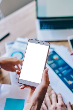 Kağıt grafik, diyagram ve dizüstü bilgisayarlı ahşap masaüstüyle arka planda internet içeriğiniz için boş ekran alanı olan modern akıllı telefonun el ele tutuşunun kırpılmış görüntüsü.