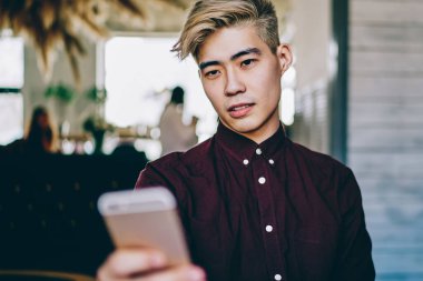 Japon hipster adam akıllı telefon cihazında uygulama bildirimi okuyor, Asyalı erkek blogcu modern cep telefonuyla interneti taramak için 4G kablosuz kullanıyor.