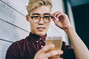 Asyalı hippi blogcu, internet sitesinde, duvarın yanında duran 4G interneti kullanarak haber okuyor. Akıllı telefondan sosyal ağlarda günlük kıyafetlerle sohbet eden Çinli genç adam.