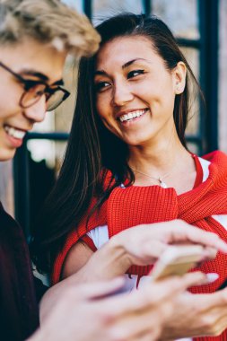 Sıradan giyinmiş neşeli Çinli hippi adamlar gülüyor ve akıllı telefonlarda komik profilleri tartışıyorlar şehir ortamında ayakta duruyorlar. Hücresel uygulamadan bahseden pozitif Asyalı arkadaşlar.