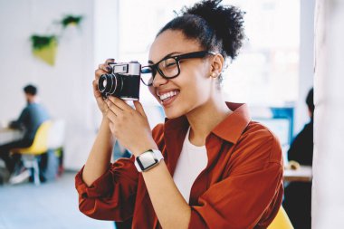 Vintage kamera ile fotoğraf yapma optik gözlük neşeli kadın amatör fotoğrafçı, karanlık tenli pozitif kadın hobi için zaman zevk eski moda ekipman kapalı kullanarak fotoğraf çekmek