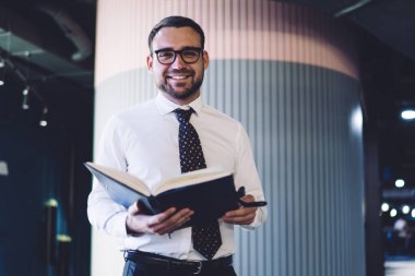 Şirket ofisinde iyi hissetmeyi planlayan neşeli muhasebecinin yarım boy portresi, çalışma alanında kameraya gülümseyen gözler için optik gözlük takan neşeli adam.
