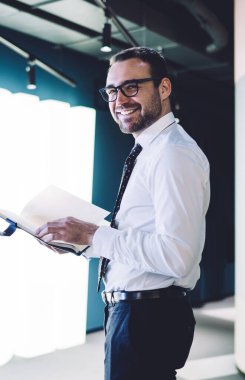 Kafkas gururlu CEO 'nun yarım boy portresi iş günü boyunca mutlu hisseder. Kameraya planlama ve gülümseme kitapçığı tutar. Gözlüklü olumlu bir adam 30 yaşında atölyede durur.