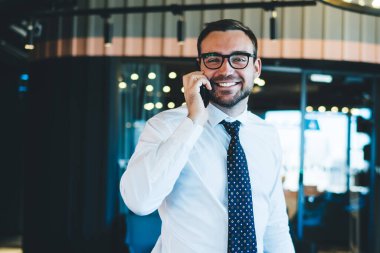 Resmi beyaz gömlekli heyecanlı bir şirket çalışanının yarım boy portresi. Fotoğraf makinesine gülümsüyor, örgüt için ders kitabı tutuyor ve akıllı telefon görüşmesi yapıyor. Cep telefonunu telefonla arayan mutlu adam.