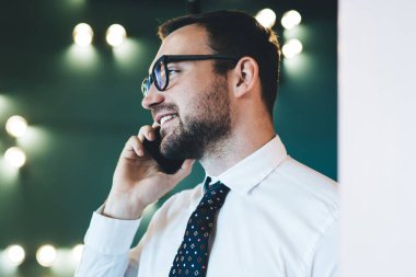 Dijital akıllı telefondaki 4G bağlantısını kullanarak sohbetten keyif alan başarılı, neşeli adam yönetmenin yan görüntüsü, iş molasında koridorda dururken cep telefonuyla konuşan erkek ekonomist