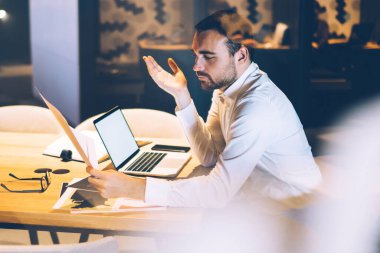Kağıt raporundan bilgi okuyan kafası karışmış işadamlarının yan bakışı, masaüstü bilgisayarı ve tanıtım alanı olan verileri analiz ederken, girişimdeki dijital pazarlama kavramını da göz önünde bulundurun.