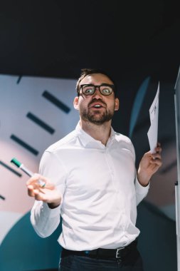 Toplantı odasında sunum yapmak için çalışırken kameraya bakan hayret içindeki işadamının yarı boy portresi, göz koruması için optik gözlük takan harika erkek simsar.