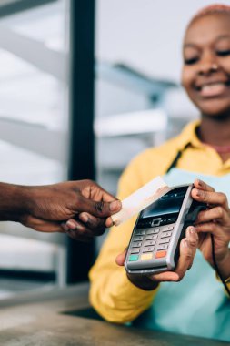 Modern kafeden yemek alırken ödeme terminalinin yanında isimsiz bir siyah adamın eli temassız kredi kartı tutuyor.