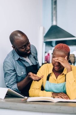 Önlüklü Afro-Amerikalı bir adam, küçük bir kahve dükkanının muhasebe kayıtlarını tutarken ve tezgahın arkasında beklerken yorgun meslektaşıyla cesaretlendirici bir şekilde konuşuyor.