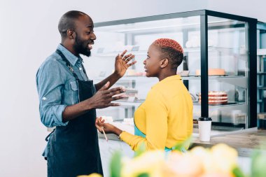Afro-Amerikalı kadın ve erkeğin yan görüntüsü gülümsüyor ve restoranda birbirleriyle sohbet ederken hoş sohbetler ediyorlar.