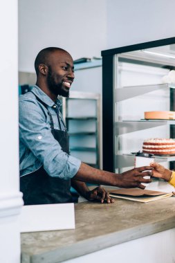 Yakışıklı, Afro-Amerikan bir adamın gülümsemesi ve kahve evinde çalışırken çekici siyahi bir kadına sıcak içecek vermesi.