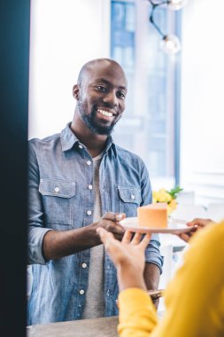Yakışıklı Afro-Amerikan erkek, gülümsüyor ve küçük kafede sipariş verirken isimsiz kadın baristadan lezzetli bir parça alıyor.