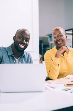 Yakışıklı Afro-Amerikan erkek ve çekici siyah kadın. Arkadaşça gülümseyen ve kafeteryada oturmuş kameraya bakan ve birlikte proje üzerinde çalışan.