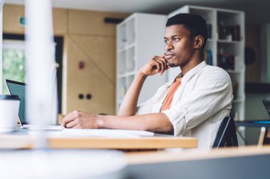 Modern ışık ofisindeki masada oturan yakışıklı siyahi adamın yan görünüşü ilham ve tefekkür ile gözlerini kaçırıyor.