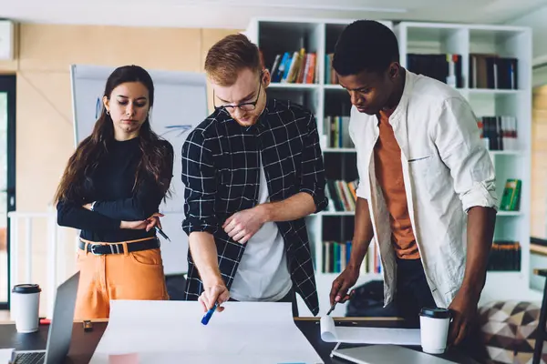 Çağdaş ofiste masa başında duran kağıt üzerine plan çizerken, modern kadın ve erkekler stratejilerini tartışıyor.