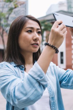 Asyalı kadın cep telefonuyla görüntülü şehir görüşünü alıp sokak ortamında dururken cep telefonuyla sohbet ediyor, kadın cep telefonu tutuyor ve kişisel turistik web günlüğü için resimlere tıklıyor