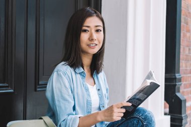 Çekici Çinli okuyucunun portresi, elinde çok satan kitaplarla ev kapısının yanında oturuyor ve oda arkadaşını bekliyor çünkü anahtarları unutuyor, edebiyat kitabı olan güzel bir kadın kameraya poz veriyor.