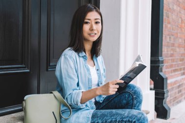 Çekici Çinli okuyucunun portresi, elinde çok satan kitaplarla ev kapısının yanında oturuyor ve oda arkadaşını bekliyor çünkü anahtarları unutuyor, edebiyat kitabı olan güzel bir kadın kameraya poz veriyor.