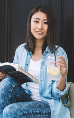 Su içeceği ile pozitif kadın okuyucunun portresi ve şehir ortamında dinlenen ilginç çok satanlar ve boş zamanlardaki kameralara gülümseme, gençlik yaşam tarzı ve hobi zamanı konsepti