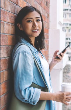 Pozitif Çinli kadın blog yazarının yarım boy portresi açık havada kahve molası ve takipçilerle online iletişimin keyfini çıkarıyor, cep telefonuna gülümseyen mutlu Asyalı kadın.