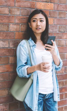 Gündelik giyinmiş düşünceli bayan öğrenci sosyal web yayını yaratırken ve ilginç içerik metni, modern teknoloji kavramı üzerinde düşünürken başka yöne bakıyor.