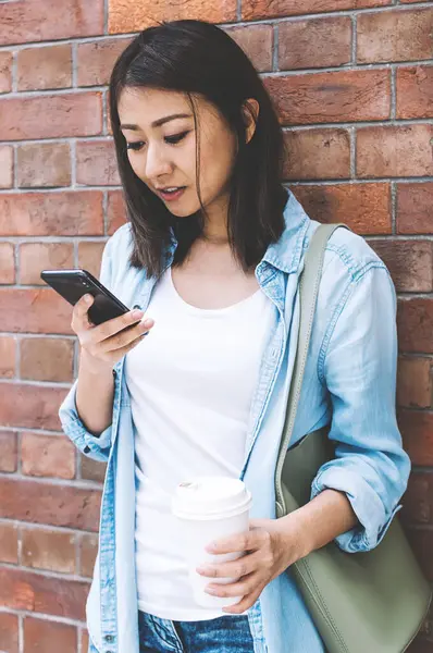 Genç Asyalı hippi kız arkadaşlarıyla internet üzerinden iletişim kurarken cep telefonuna mesaj yazıyor. Eğitim için internet bilgilerini arayan çekici uluslararası kız öğrenci.