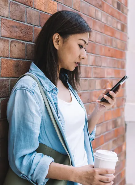 Cep telefonuyla internet sitesinden bilgi arayan bir fincan kafein içeceği ile gezen Çinli turist, cep telefonuyla şehirlerde zaman geçiren Çinli yeniyetme kız.