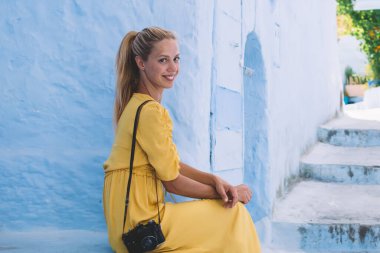 Chaouen binası yakınlarında dinlenen neşeli kadın turistin portresi ve kameraya gülümseyen Fas 'a yaz gezisinin tadını çıkaran, antik şehirleri keşfeden klasik kameralı mutlu bir kadın.