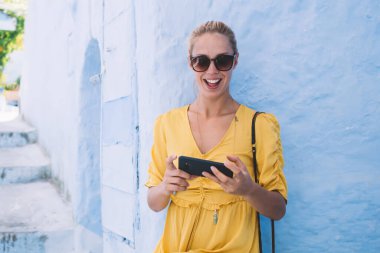 İnternetten haberleşmenin keyfini süren mutlu güneş gözlüklü kadın, Fas 'ta otel rezervasyonu için indirimli e-posta alınca şaşırdı, sokakta modern akıllı telefon kullanan kadın turist