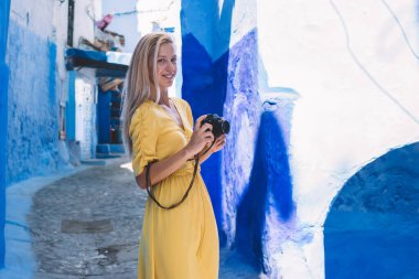 Mavi dış görünüşlü, Berber Bölgesi 'nde yaz tatiline çıkan mutlu bir kadınla şehrin göbeğinde kameralı beyaz kadın fotoğrafçının yarım boy portresi.