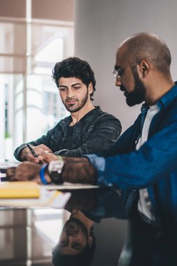 Modern barda toplanan şık etnik erkeklerin yan görünümü bilgisayar ve kağıtlarla tartışırken tezgahta oturması