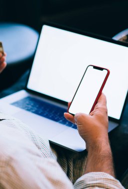 Elinde plastik kredi kartı tutan, bankacılık verilerini doğrulayan, dizüstü bilgisayardan ve telefondan online alışveriş yapan, web reklamları için boş ekran oluşturan beyaz bir genci kapatın.