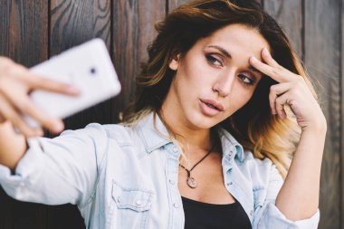 Rahat bir görünüm güzel kadın ahşap arka plan yakın boş zaman sırasında mobil web kamera görüntüleri alarak, çekici beyaz kadın Blogger sosyal ağda göndermek için kendini fotoğraflama