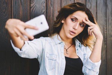 Rahat bir görünüm güzel kadın ahşap arka plan yakın boş zaman sırasında mobil web kamera görüntüleri alarak, çekici beyaz kadın Blogger sosyal ağda göndermek için kendini fotoğraflama