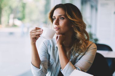 Kahve molası kapalı sırasında kafeterya penceresine bakarak düşünceli kadın düşüncelere, çay bardağı ile oturan ve edebiyat dünyasında bir sonraki en çok satıcı için yeni fikirler hakkında düşünme düşündürücü kadın yazar