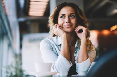 Olumlu kadın genç favori kafeteryasında boş zaman zevk uzağa bakıyor ve iyi bir gün hakkında hayal, mutlu gülümseyen kadın 20s rahat bakmak giyinmiş kafede masada oturan