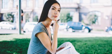 Tasarım projesi için fikirler hakkında düşünme sırasında açık havada görünümlü düşünceli kadın öğrenci durulması, zarif beyaz hipster kız yaz parkında eğitim için ders kitabı ile oturuyor