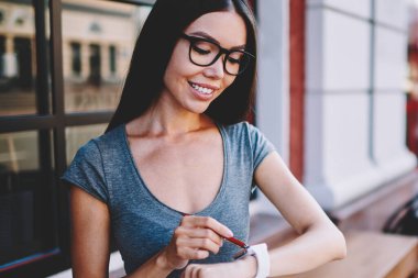Sokak kafeteryasında röportaj bekleyen ve elektronik SmartWatch 'da zaman kontrol eden mutlu kadın gazeteci, optik gözlükler içinde pozitif hipster kız giyilebilir kol saati üzerinde bildirim güncelleme