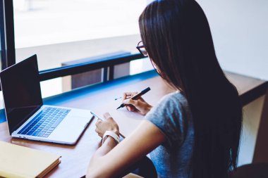 Dizüstü bilgisayar uygulama yoluyla şirket için multimedya dosyaları oluşturmak için yaratıcı kadın grafik tasarımcı çizim skeçler arka görünümü, kadın web sitesinde halk içerik makalesi için notlar yapma