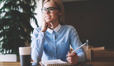 Eğitim için ders kitabı ile masada otururken üniversite projesi için fikirler hakkında olumlu öğrenci mimar düşünme, gözlüklü başarılı hipster kız kolej kampüs bakıyor