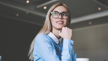 Çekici hipster kız düşünceliye bakarak üniversite masasında fincan ve ders çalışmaları hakkında düşünme, üniversite ödevleri üzerinde durulması şık gözlükler içinde dalgın kadın öğrenci otururken