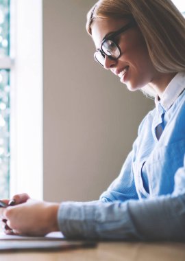 Okul sınıfta oturan gözlüklü mutlu öğrenci kız cep telefonu ile Web sayfasında e-posta ve okuma haberleri kontrol, olumlu kadın arkadaşlarınızla online modern smartphone kullanarak sohbet